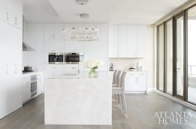White modern kitchen with marble island, integrated appliances, and crystal chandelier.