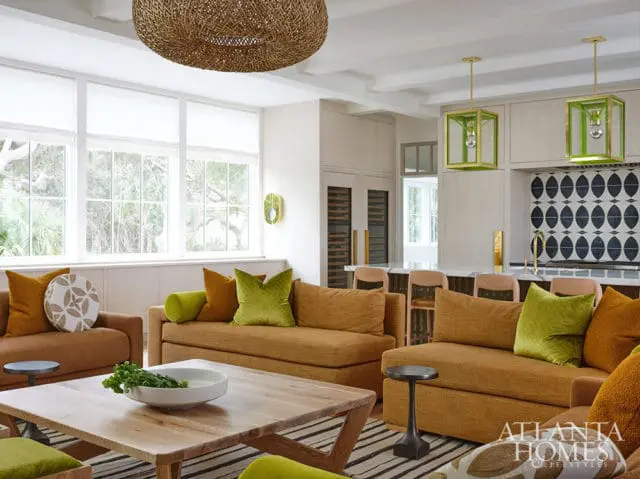 Living room with mustard sofas, green pillows, wood coffee table, and patterned backsplash.