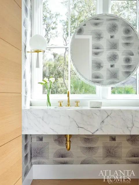 Marble vanity with brass fixtures and geometric wallpaper.