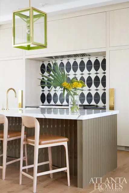 Kitchen island with marble countertop, fluted olive green base, and leather stools. Black and white