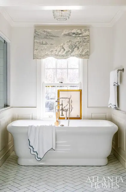 White freestanding bathtub with a cloud-patterned valance above the window and herringbone tile