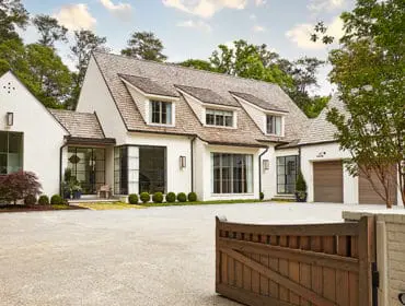 White brick house with wood shake roof, large windows, and a three-car garage.