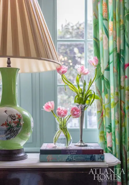 Green lamp with bird motif, pink tulips in vases on books, and floral curtains