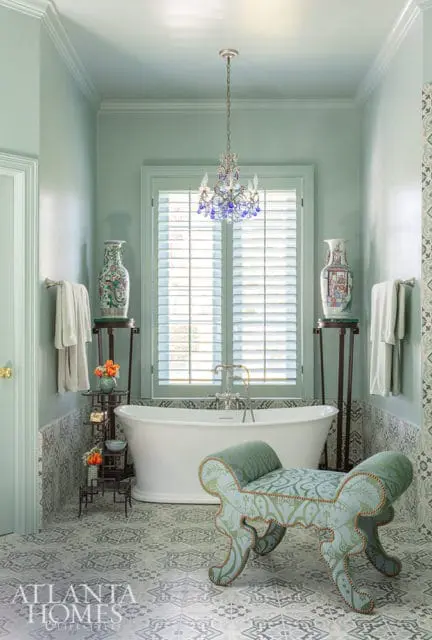 Pale green bathroom with freestanding tub, ornate bench, and patterned tile floor