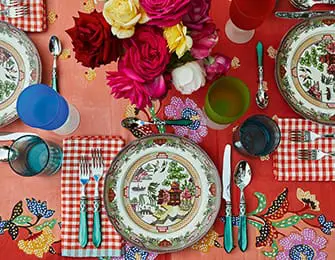 Table setting with floral plates, red gingham napkins, and colorful glassware.