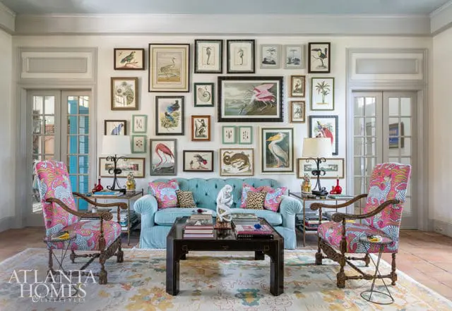 Light blue tufted sofa with patterned pillows, dark wood coffee table, and two chairs with pink and