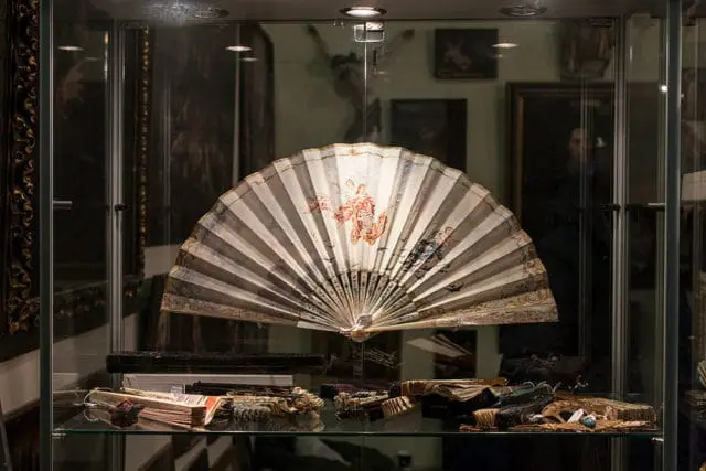 Antique fan with painted figures displayed in a glass case