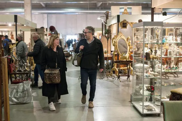 Couple browsing an antique market with display cases and ornate furniture