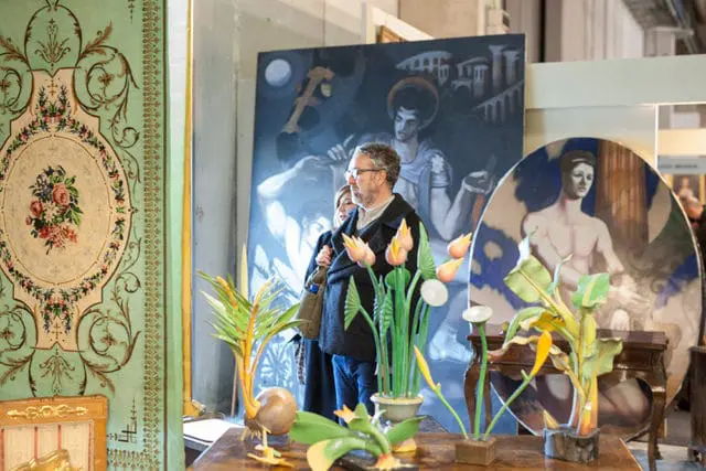Man and woman looking at paintings, with decorative floral sculptures in foreground.