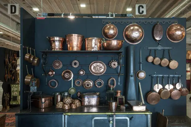 Dark blue wall display of antique copper cookware, pots, pans, and molds.