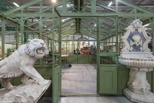 White lion statue and ornate fountain in front of a green greenhouse structure