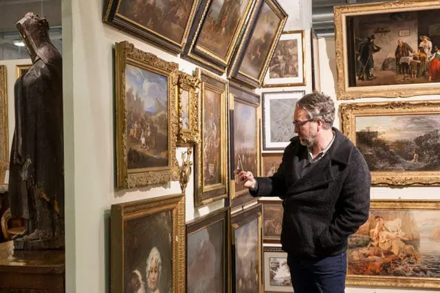 Man examining framed paintings and a statue in a gallery