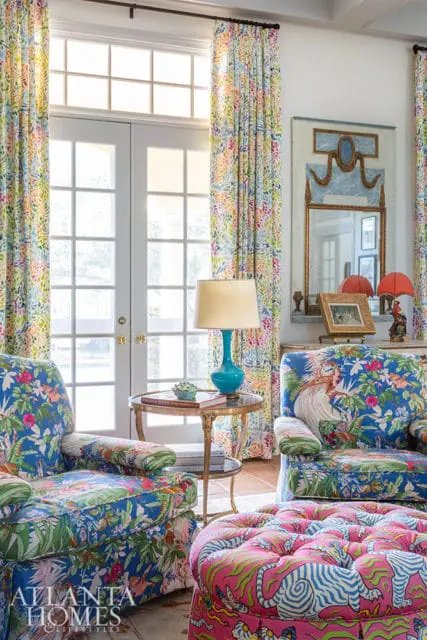 Living room with floral print chairs and ottoman, blue lamp, and patterned curtains.