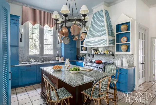 Blue kitchen with granite island, copper pots, and striped valance over window.