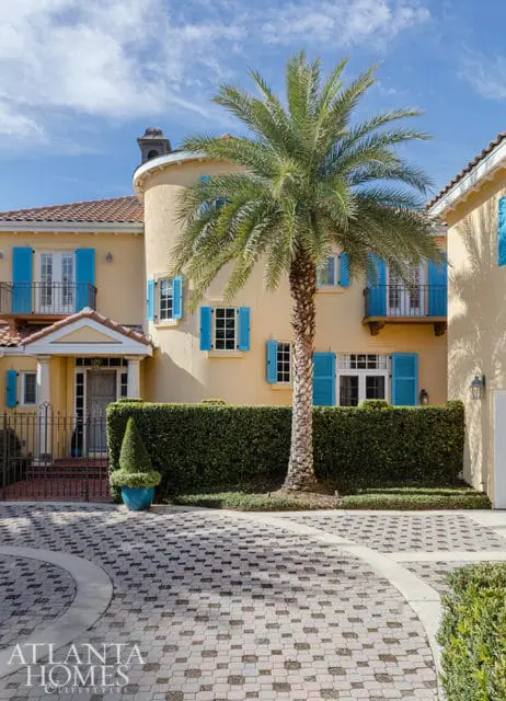 Yellow house with blue shutters, palm tree, and paved driveway.
