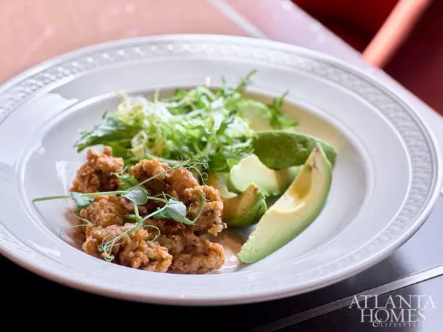 Fried chicken pieces with avocado slices and salad on a white plate.