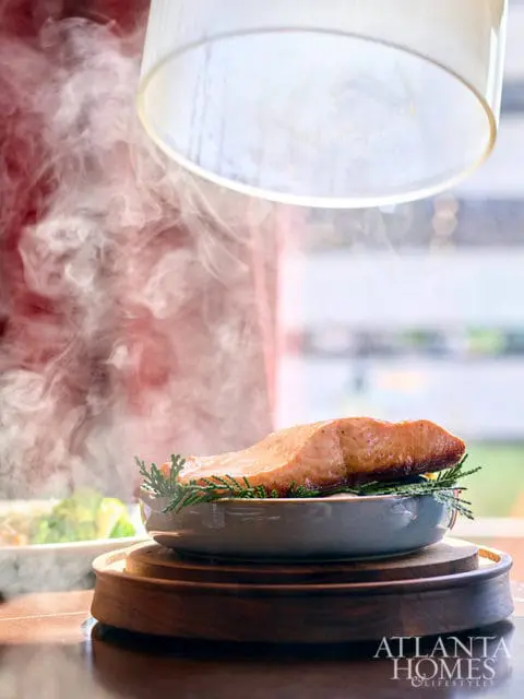 Steaming salmon fillet on a bed of rosemary in a gray bowl on a wooden stand