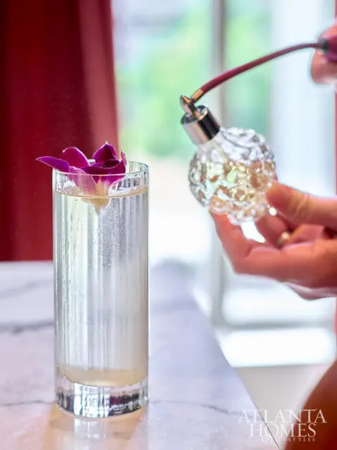 Glass perfume atomizer spraying a drink with purple orchid petals