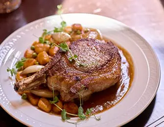Pork chop with gnocchi, peas, and carrots in brown sauce on white plate