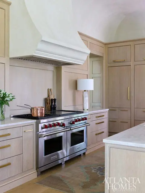 Light wood kitchen with stainless steel Wolf range, marble countertops, and brass hardware.