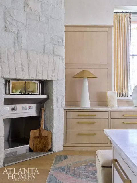 Stone fireplace with built-in oven, wood cabinets with brass hardware, and patterned rug.