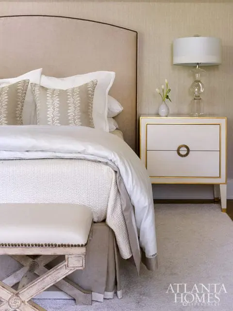 Bedroom with upholstered headboard, patterned pillows, and white nightstand with gold trim