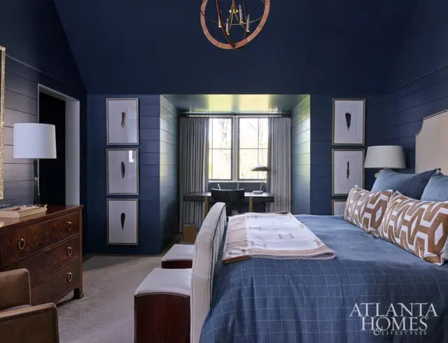 Bedroom with navy blue walls, shiplap detail, and framed feather art. Bed has blue plaid bedding.