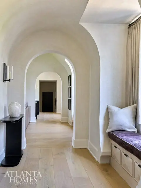 Hallway with arched doorways, light wood floors, and a built-in bench with purple cushion.