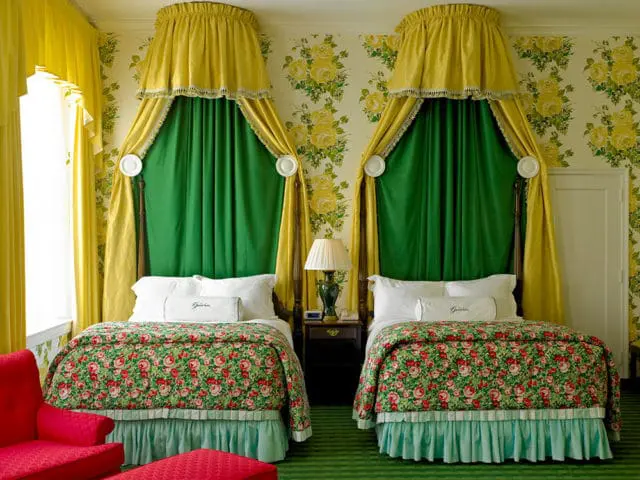 Bedroom with two beds, yellow canopy drapes, green curtains, floral comforters, and floral