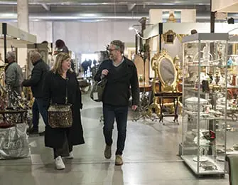 Couple walking through an antique market with ornate furniture and display cases