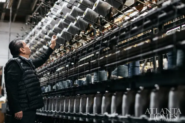 Man inspecting rows of spools of thread on industrial machinery.