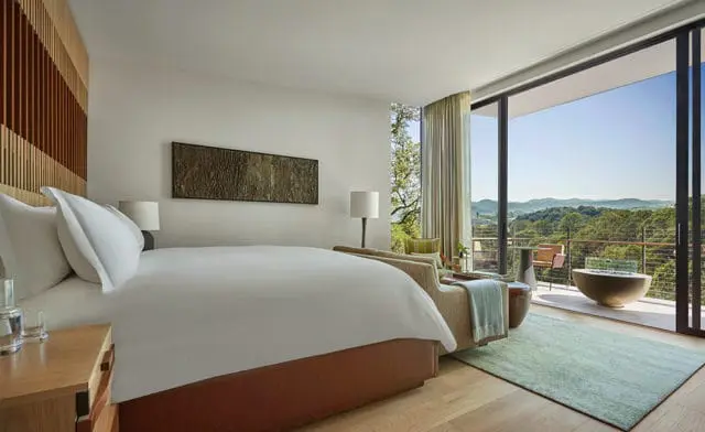 Bedroom with white bedding, wood accent wall, and mountain view from balcony.
