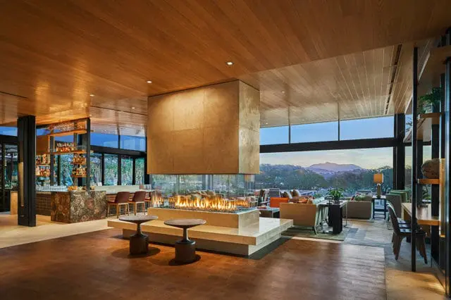 Modern lobby with a large stone fireplace, bar area, and seating overlooking a mountain view.