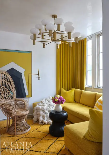 Yellow living room with sectional sofa, wicker chair, abstract art, and brass chandelier.