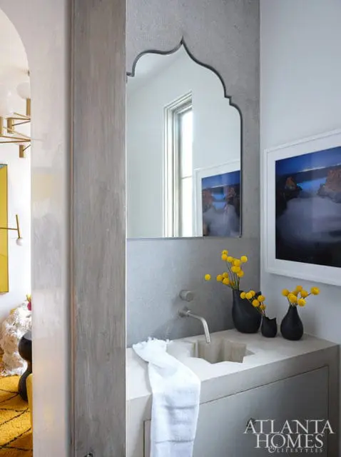 Powder room with concrete sink, arched mirror, and framed art. Yellow flowers in black vases.