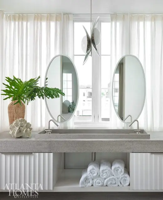 Modern bathroom with double oval mirrors, concrete vanity, and fluted white cabinets.
