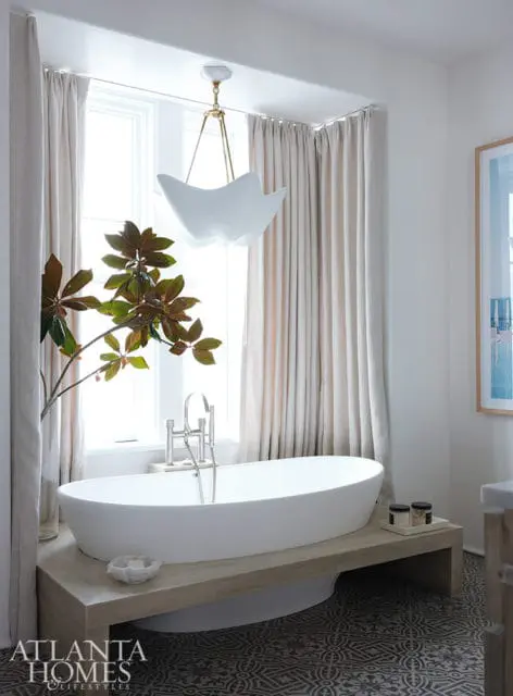 White freestanding bathtub on a wooden platform with a modern chandelier above.