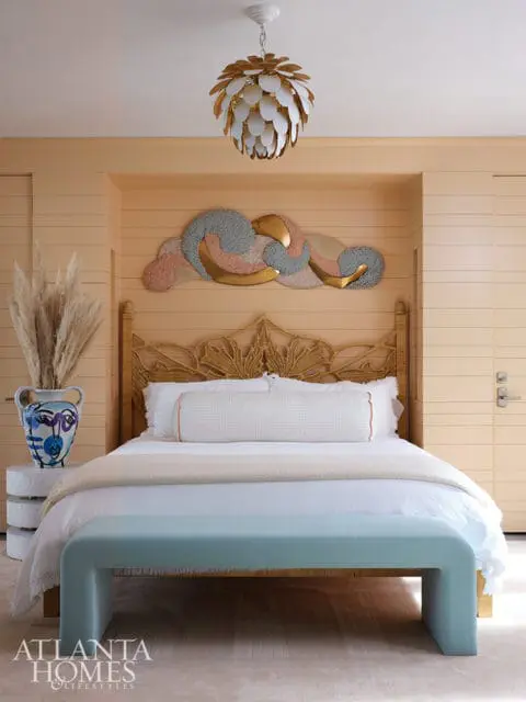 Bedroom with light peach walls, rattan headboard, white bedding, and a pale blue bench.