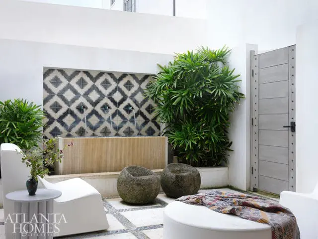 White lounge chairs and ottoman on tiled patio with fountain and gray door