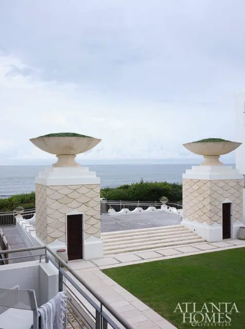 Stone pillars with grass-filled urns overlook the ocean, with a patio and lawn in the foreground.