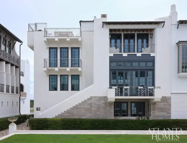 White modern house with dark windows, balconies, and stairs. Atlanta Homes & Lifestyles logo.
