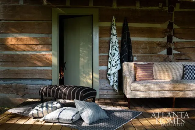 Sofa and bench on wooden porch with pillows and textiles against log wall