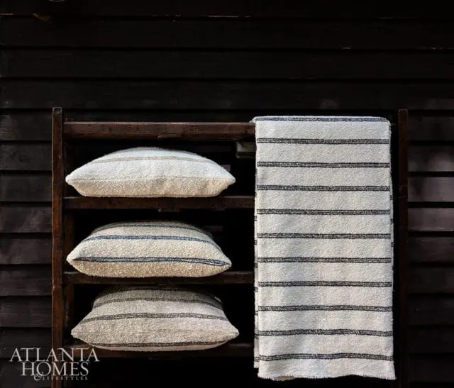 Three textured pillows and a striped towel on a wooden shelf against a dark wood wall.
