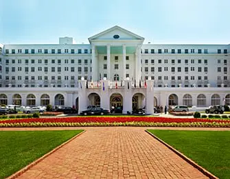 Grand white hotel with columns and arched entrance, manicured lawn, and flower beds