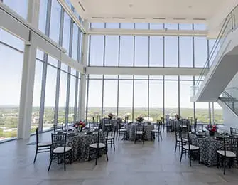 Event space with floor-to-ceiling windows overlooking a city, set tables with black and white