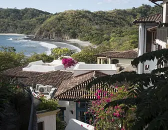 Spanish colonial style buildings with red tile roofs overlooking a tropical beach and lush green