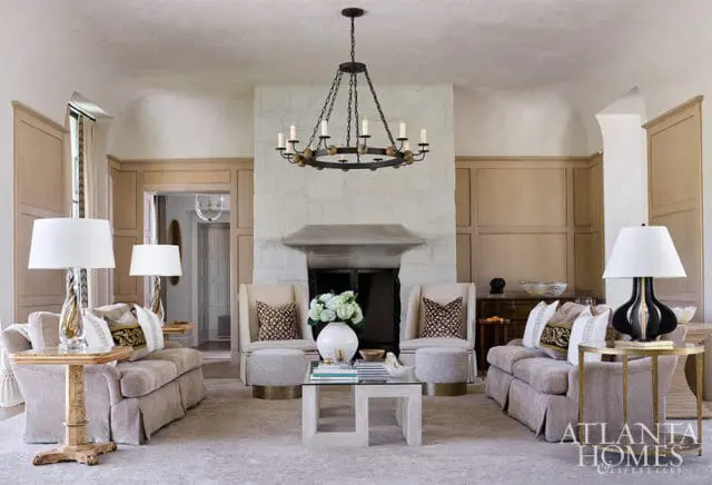 Living room with stone fireplace, neutral sofas, wood paneling, and Atlanta Homes & Lifestyles logo.