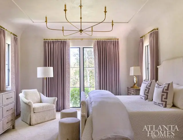 Bedroom with lavender curtains, upholstered chair, and gold chandelier.