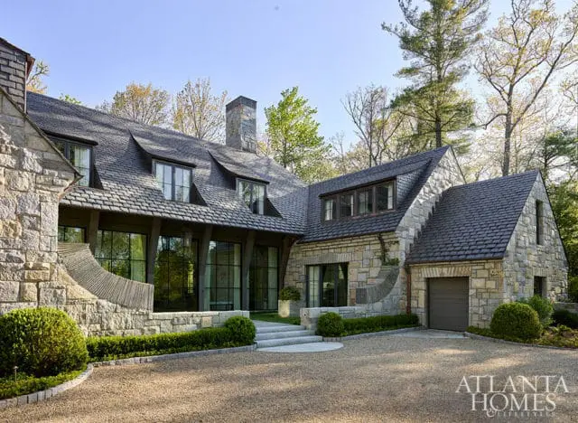 Stone house with dark shingle roof, dormer windows, and attached garage.