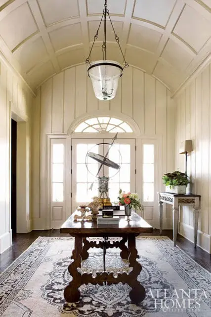 Foyer with paneled ceiling, arched doorway, console table with decorative objects, and ornate rug.
